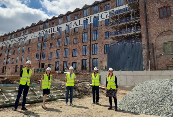 A photograph of five people stood in front of a five-storey brick mill building